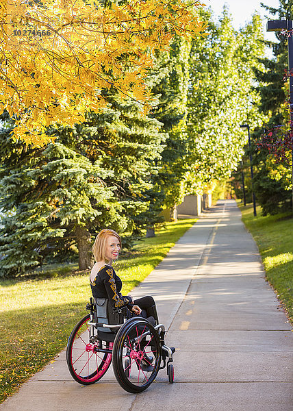 Junge querschnittsgelähmte Frau in ihrem Rollstuhl auf einem Weg in einem Stadtpark im Herbst; Edmonton  Alberta  Kanada'.
