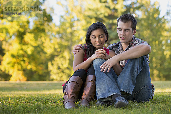 Gemischtrassiges Paar beim gemeinsamen Gebet in einem Park im Herbst; St. Albert  Alberta  Kanada'.
