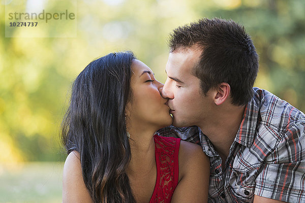 Gemischtrassiges Paar küsst sich in einem Park im Herbst; St. Albert  Alberta  Kanada'.