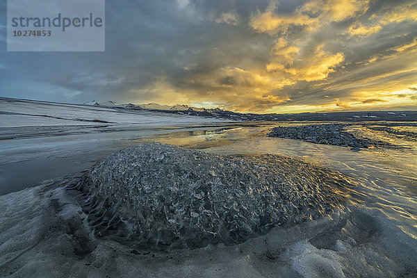 Der Sonnenaufgang erhellt den Himmel über einem zu einem Fluss gefrorenen Eisberg an der Südküste Islands; Island