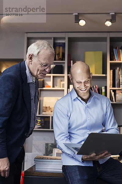 Glückliche Geschäftsleute  die gemeinsam im Büro den Laptop benutzen