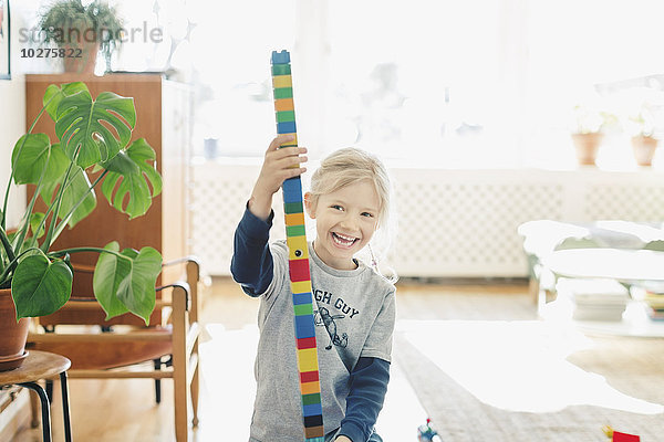 Fröhliches Mädchen hält Turm aus Spielzeugblöcken zu Hause