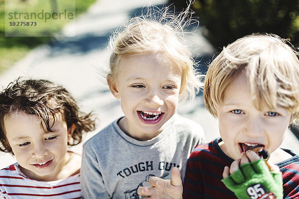 Porträt eines glücklichen Jungen  der Eis isst  während er mit Freunden auf dem Hof spazieren geht.