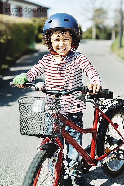 Porträt eines glücklichen Jungen  der mit dem Fahrrad auf dem Gehweg auf dem Hof steht