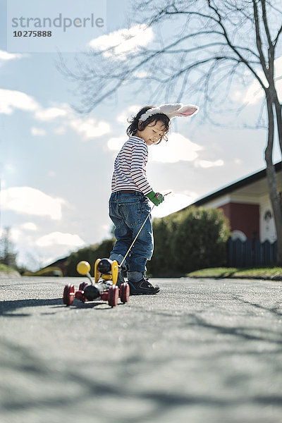 Volle Länge des Jungen  der Spielzeugauto auf dem Gehweg am Hof zieht.