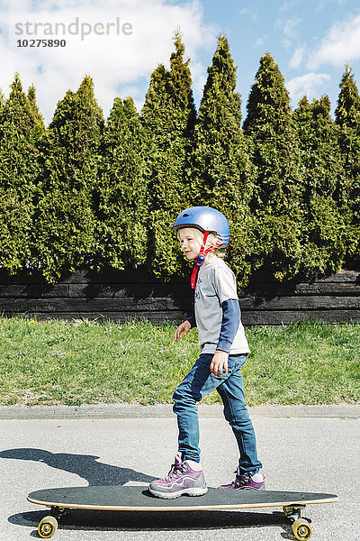 Durchgehende Seitenansicht des Mädchen-Skateboards auf dem Fußweg am Hof