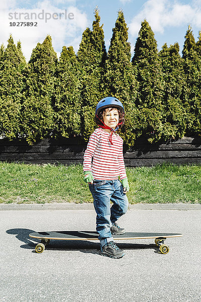 Porträt eines selbstbewussten Jungen mit Skateboard auf dem Gehweg am Hof