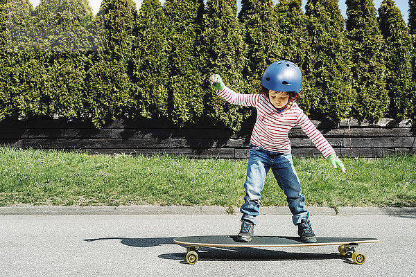 Volle Länge des Jungen  der auf dem Skateboard auf dem Hof balanciert.