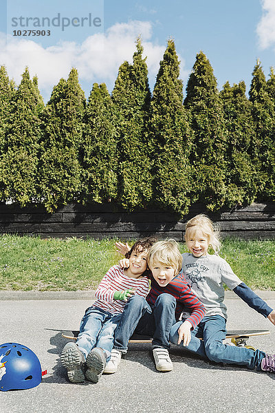 Porträt von glücklichen Jungen und Mädchen auf dem Skateboard gegen Bäume