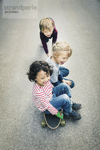 Hochwinkelansicht der Kinder beim Sitzen auf dem Skateboard