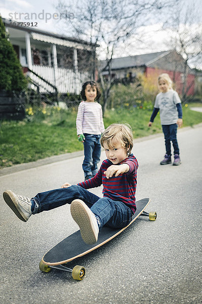 Kinder beim Betrachten des Freundes Skateboard auf dem Fußweg vor dem Haus