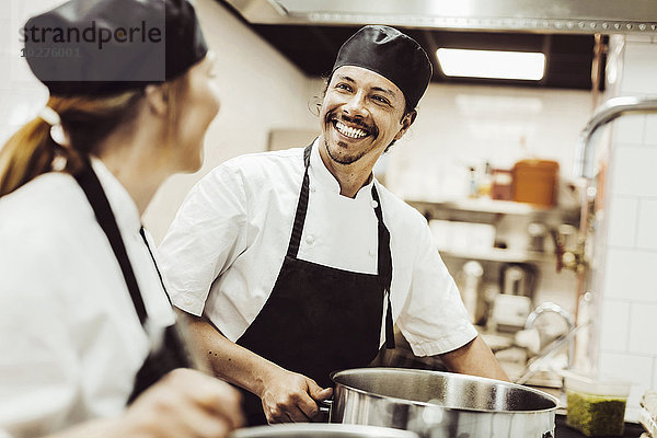 Fröhlicher Koch  der beim Kochen in der Küche Kollegen ansieht