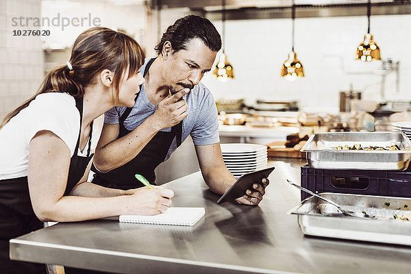 Köche und Köchinnen mit digitalen Tabletts beim Schreiben von Rezepten an der Großküchentheke