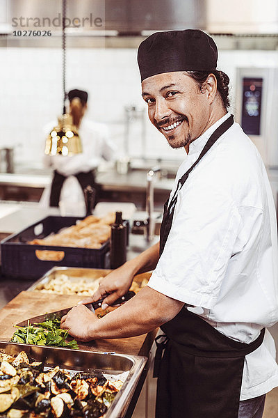 Seitenansicht Porträt eines glücklichen Küchenchefs beim Schneiden von Blattgemüse in der Großküche
