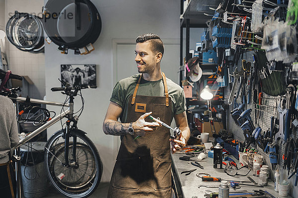 Lächelnder Mechaniker schaut Kollegen bei der Pedalreparatur in der Werkstatt an