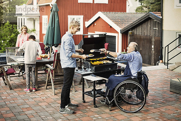 Behinderter Mann  der dem Sohn auf dem Hof gegrilltes Essen serviert.