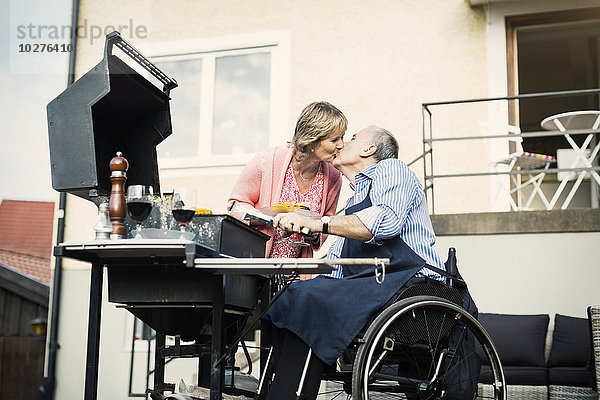 Behinderter Mann im Rollstuhl küssende Frau beim Grillen auf dem Hof
