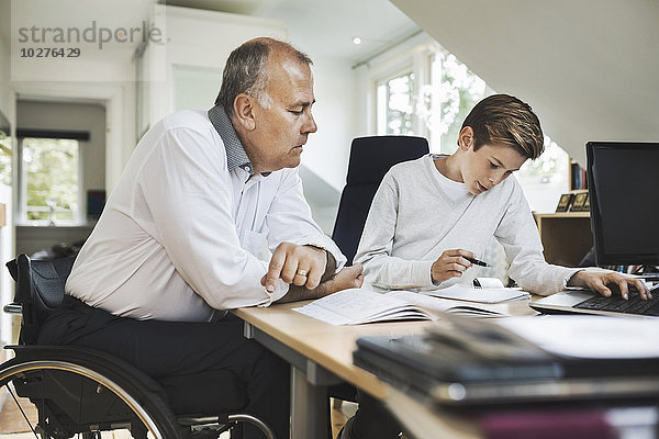 Behinderter Vater hilft dem Sohn bei den Hausaufgaben zu Hause