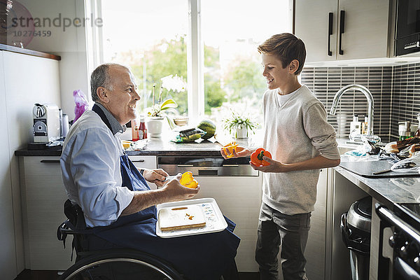 Glücklicher behinderter Vater im Rollstuhl bei der Zubereitung des Essens mit Sohn in der Küche