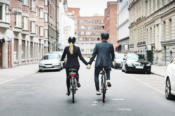 Rückansicht von Geschäftsleuten  die sich beim Radfahren auf der Straße an den Händen halten.