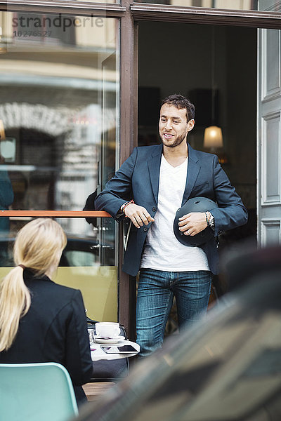 Lächelnder Geschäftsmann mit Helm beim Gespräch mit Kollegen im Straßencafé