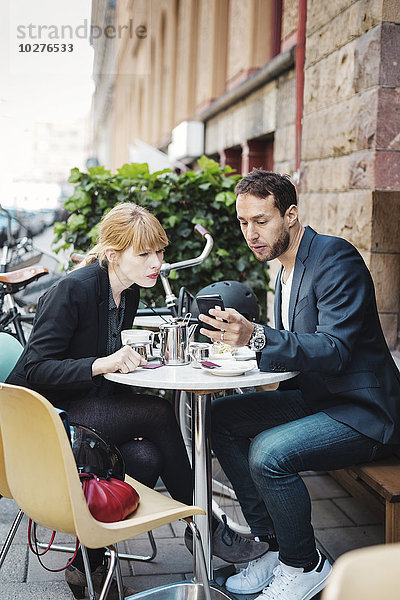 Geschäftsreisende mit Smartphone im Straßencafé