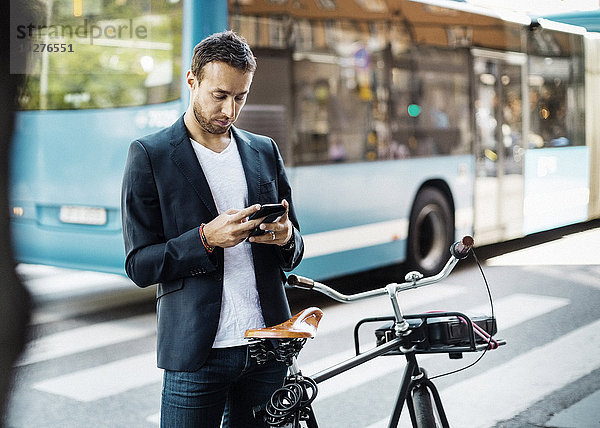 Geschäftsmann mit Handy im Stehen mit dem Fahrrad auf der Stadtstraße