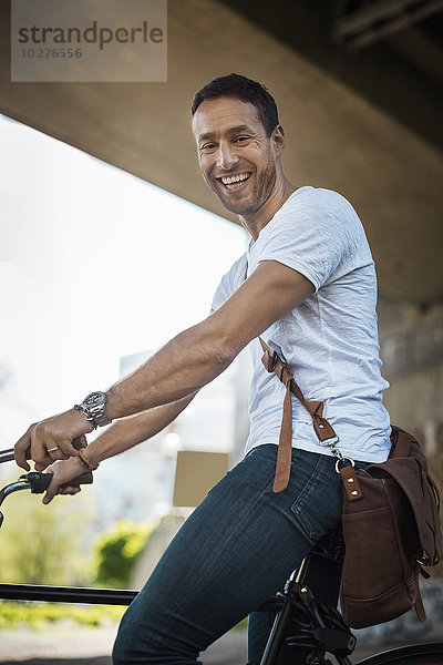 Portrait eines glücklichen Geschäftsmannes mit Fahrrad unter der Brücke