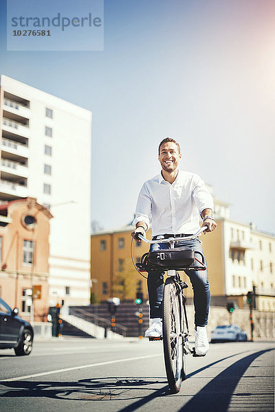 Glücklicher Geschäftsmann beim Radfahren auf der Stadtstraße gegen den blauen Himmel