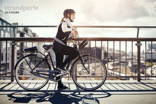 Seitenansicht der Geschäftsfrau mit auf der Brücke stehendem Fahrrad