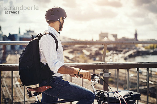 Geschäftsmann mit Fahrrad und Blick auf die Stadt  während er auf der Brücke steht.