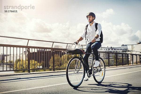 Geschäftsmann mit dem Fahrrad auf der Brücke gegen den Himmel