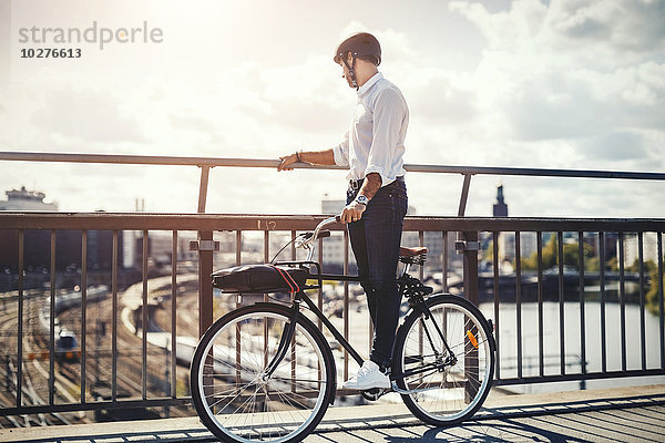 Geschäftsmann mit Blick auf die Stadt im Stehen auf dem Fahrrad