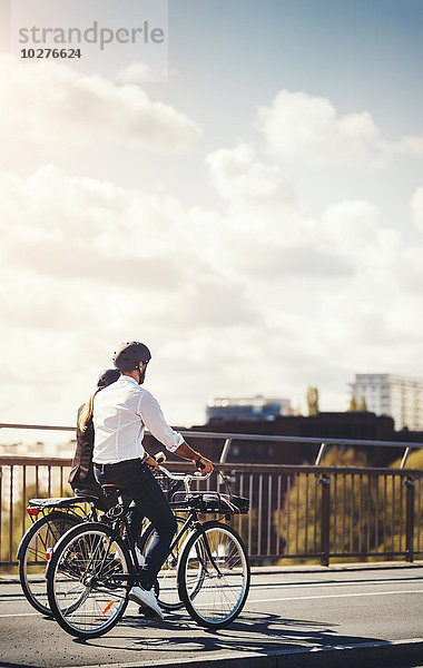 Rückansicht von Geschäftsleuten  die mit dem Fahrrad auf der Brücke gegen den Himmel fahren