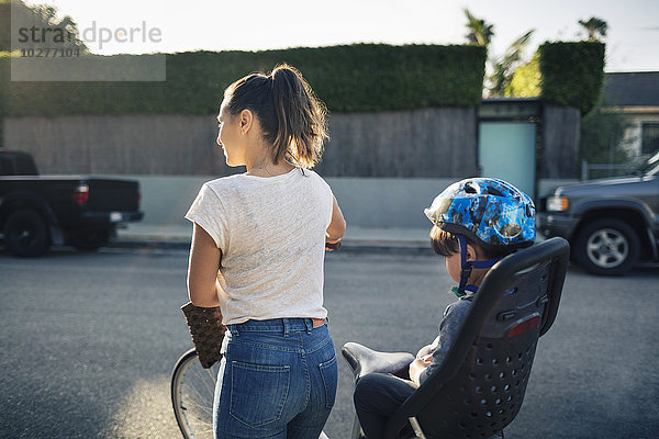 Rückansicht der Frau  die das Fahrrad hält  mit dem Sohn auf dem Rücksitz im Freien.
