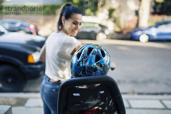 Lächelnde Frau  die ihren Sohn auf dem Fahrrad an der Straße sitzen sieht.