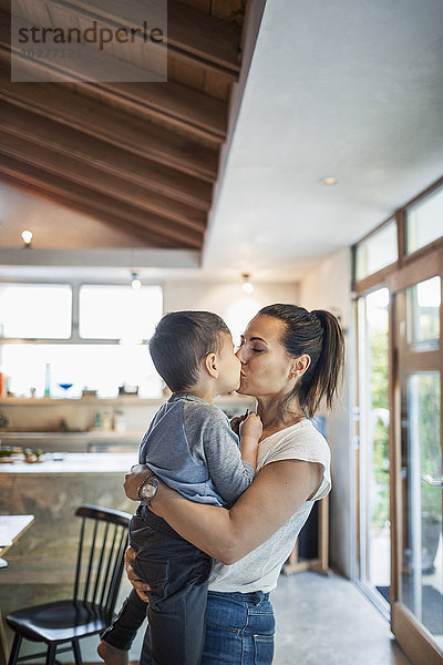 Zärtliche Frau  die ihren Sohn zu Hause küsst.
