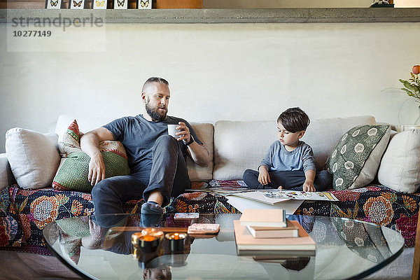 Vater hält Kaffeetasse und unterstützt den Sohn bei den Hausaufgaben zu Hause.