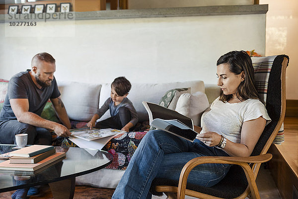 Frau liest Zeitschrift  während Vater und Sohn zu Hause im Hintergrund studieren.