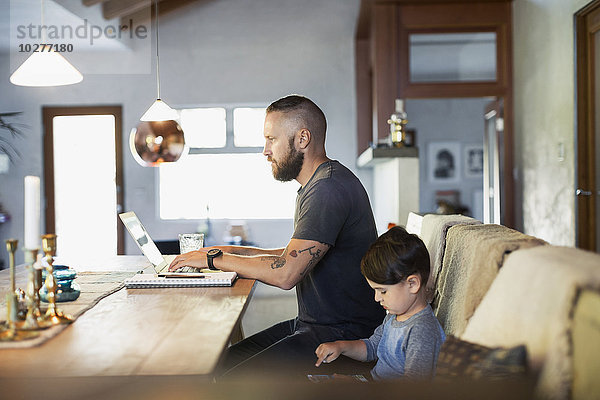 Seitenansicht von Vater und Sohn mit Technologien am Esstisch