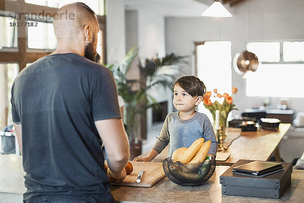Junge schaut auf Vater  der am Küchentisch steht.