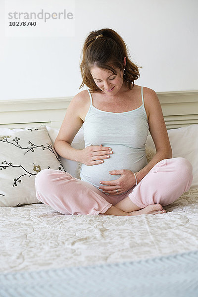 Lächelnde schwangere Frau auf dem Bett sitzend