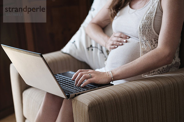 Mittelteil einer schwangeren Frau mit Laptop