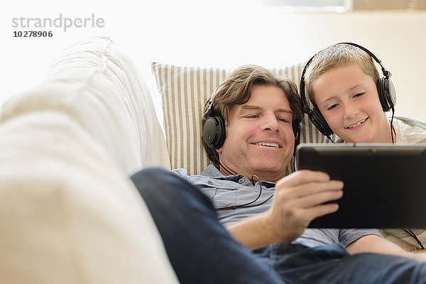 Mann benutzt Tablet-PC mit seinem Sohn (8-9) auf dem Sofa