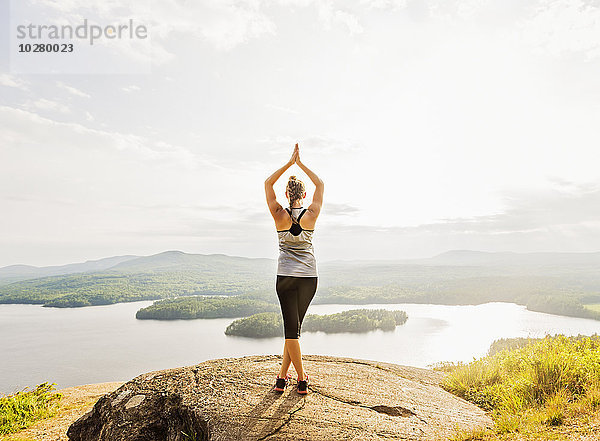 Rückansicht einer jungen Frau  die vor einem See Yoga übt