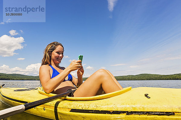 Junge Frau benutzt Smartphone im Kajak auf dem See
