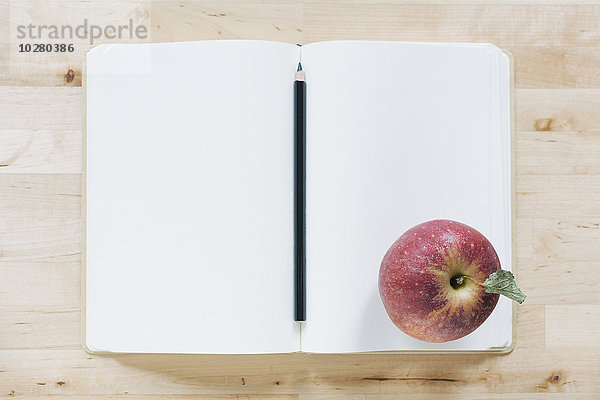 Draufsicht auf Bleistift und Apfel im Notizbuch
