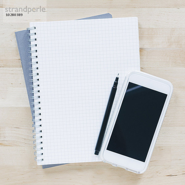 Draufsicht auf Stift und Smartphone auf einem Notizbuch