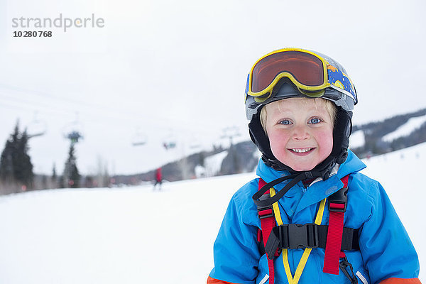 Lächelnder kleiner Junge (5) im Skianzug in den Bergen