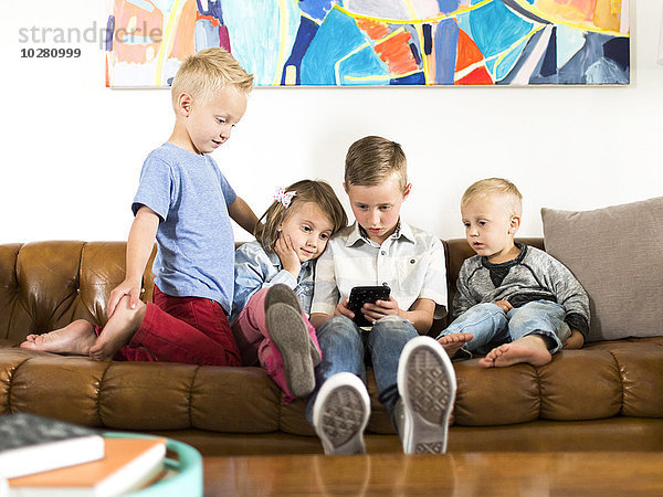 Kinder (2-3  4-5  6-7) sitzen auf dem Sofa und benutzen ihr Smartphone